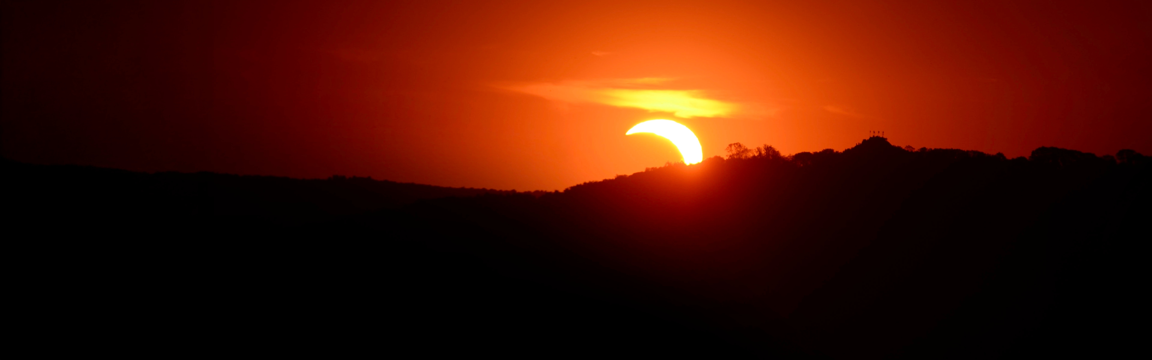 Teilweise Sonnenfinsternis hinter einem Hügel, unter einem orangefarbenen Himmel.